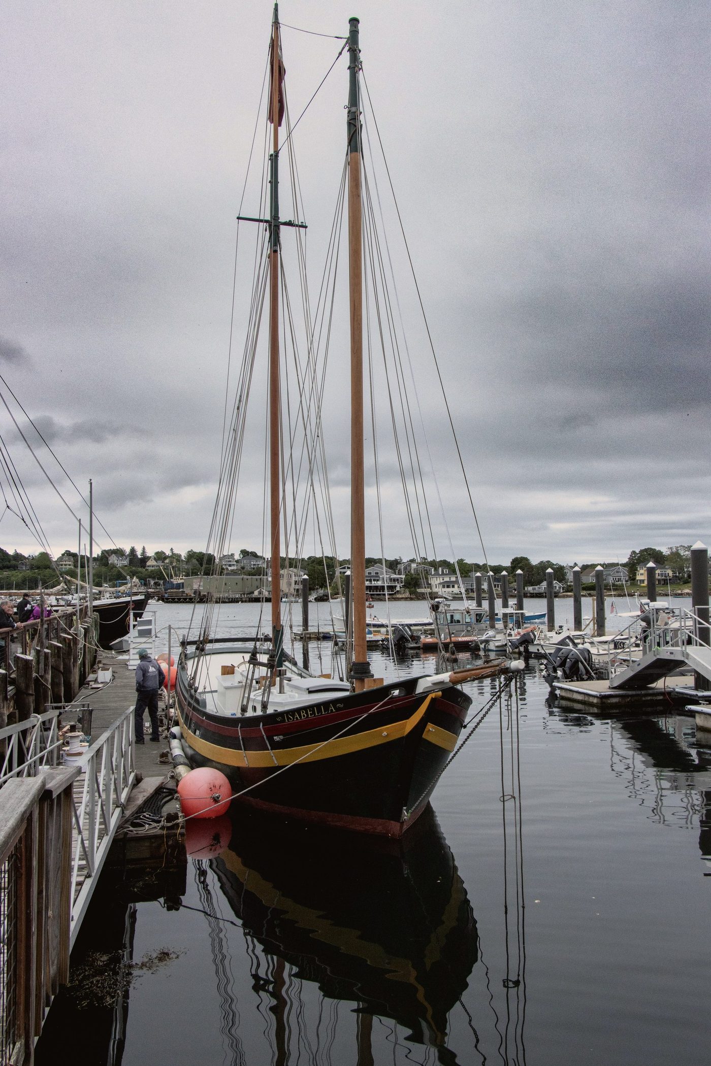 A wooden schooner moored along the working waterfront, a deckhand making fast the lines